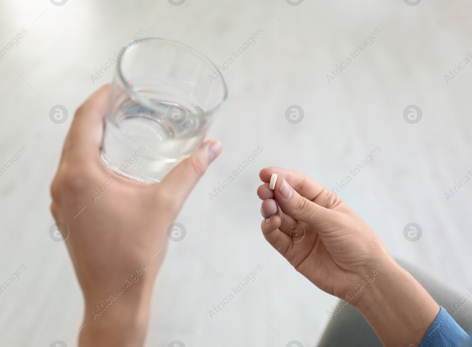 Photo of Woman holding glass of water and pill at home, closeup
