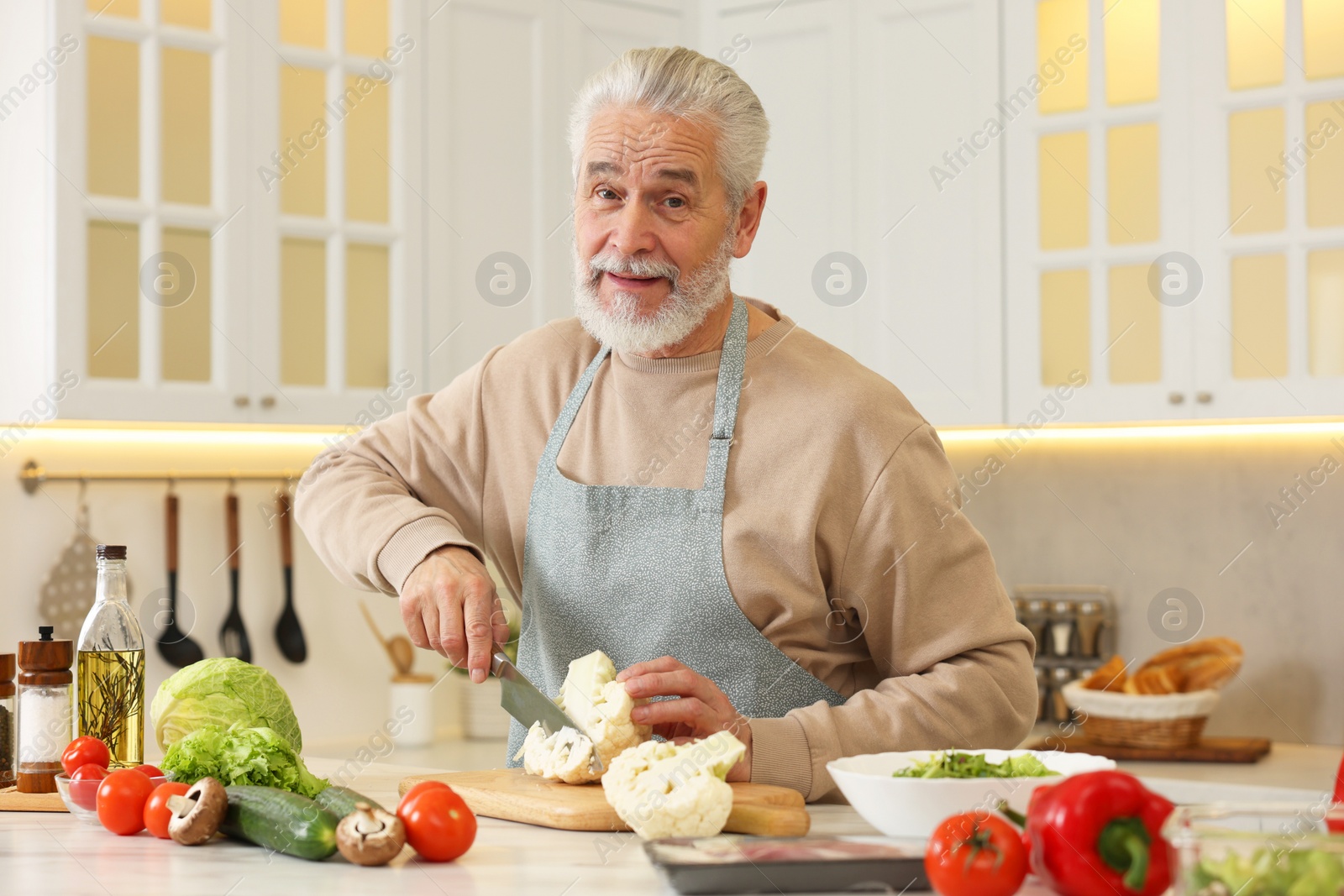 Photo of Happy man cutting cauliflower at table in kitchen