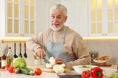 Photo of Happy man cutting cauliflower at table in kitchen