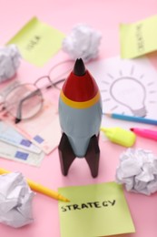 Photo of Composition with toy rocket, stationery and money on pink background, closeup. Startup concept