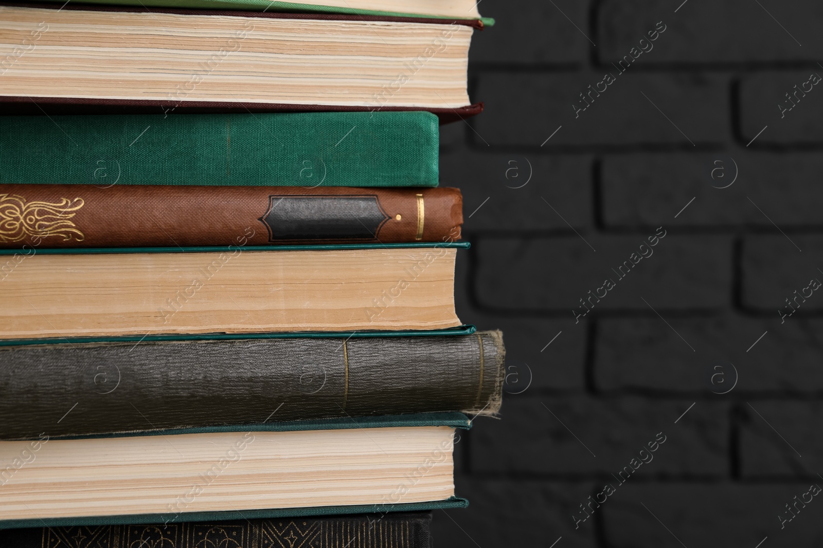 Photo of Many old hardcover books near black brick wall, closeup. Space for text