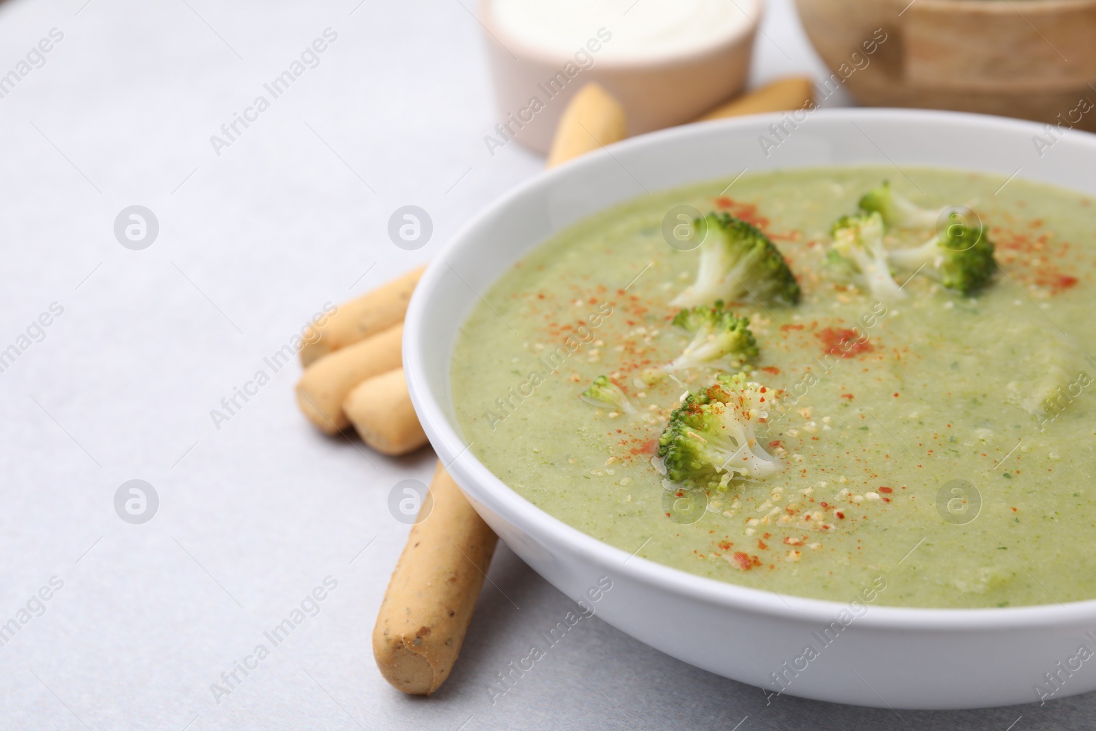 Photo of Delicious broccoli cream soup served on light table, closeup. Space for text