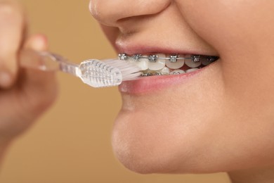 Photo of Smiling woman with dental braces cleaning teeth on brown background, closeup