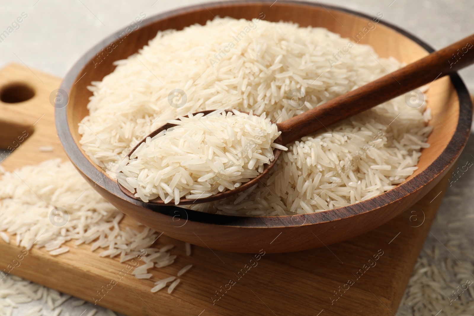 Photo of Raw basmati rice in bowl and spoon on table, closeup