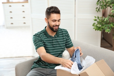 Photo of Young man opening parcel on sofa at home