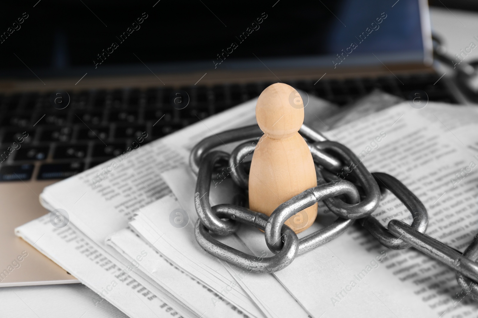 Photo of Information warfare concept. Chained wooden figure, laptop and newspapers on table, closeup