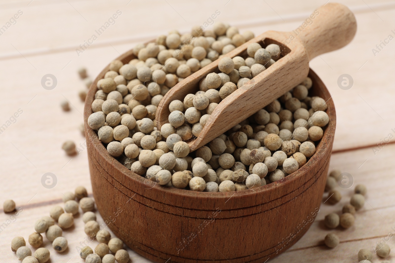 Photo of Aromatic spice. White peppers and scoop in bowl on wooden table, closeup