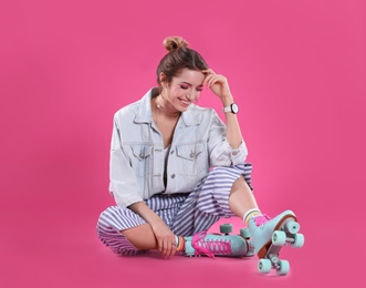 Young woman with retro roller skates on color background