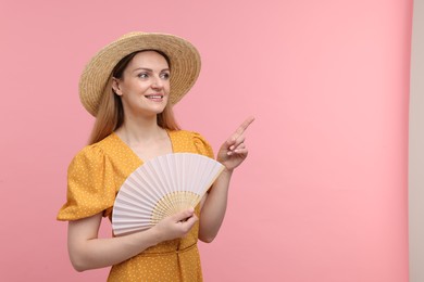 Happy woman with hand fan pointing on pink background