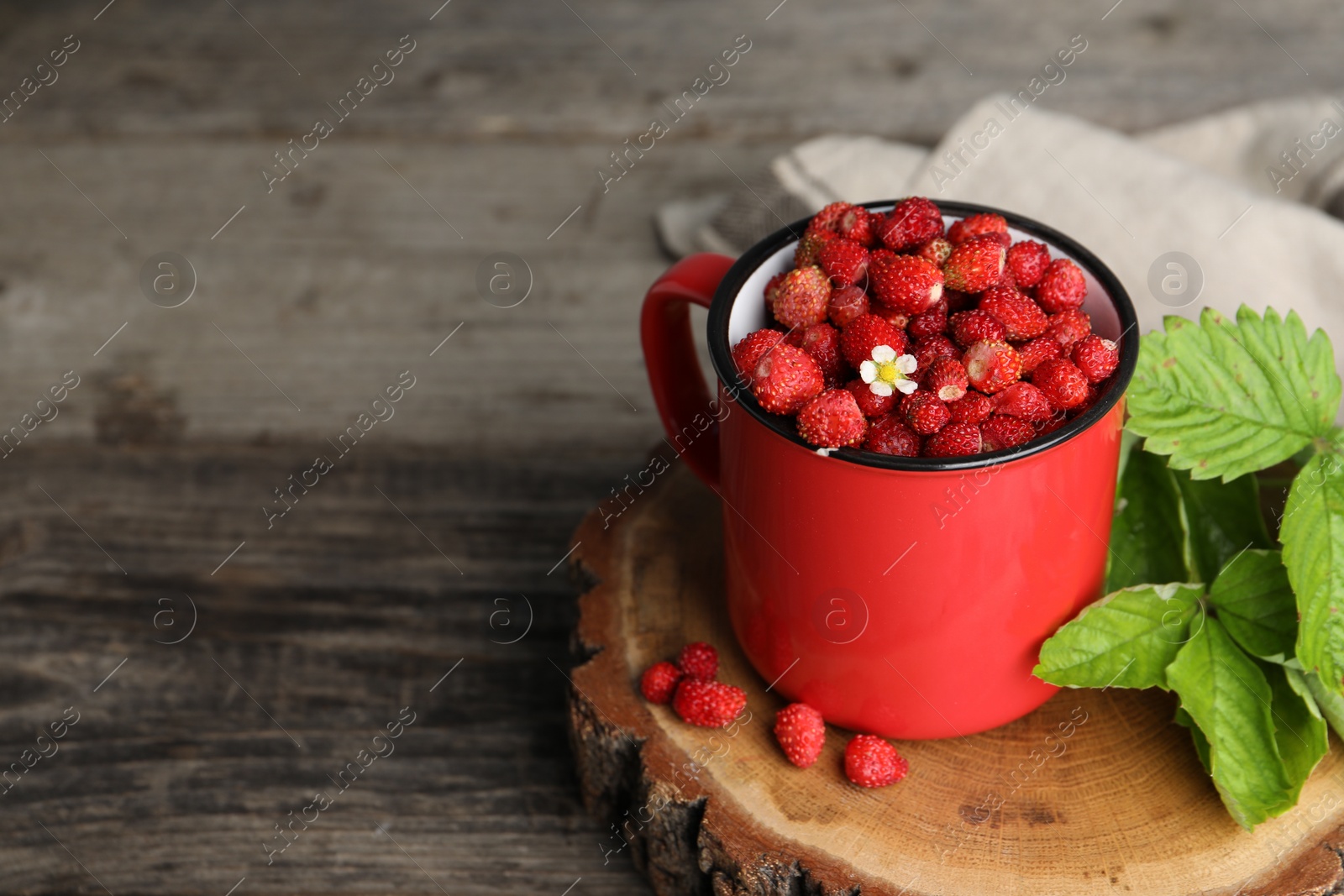 Photo of Fresh wild strawberries in mug and leaves on wooden table. Space for text