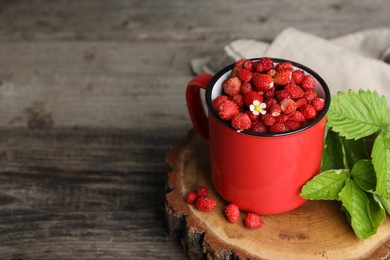 Fresh wild strawberries in mug and leaves on wooden table. Space for text