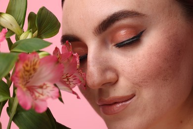 Photo of Beautiful woman with fake freckles and flowers on pink background, closeup