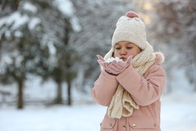 Cute little girl blowing snow in park on winter day, space for text