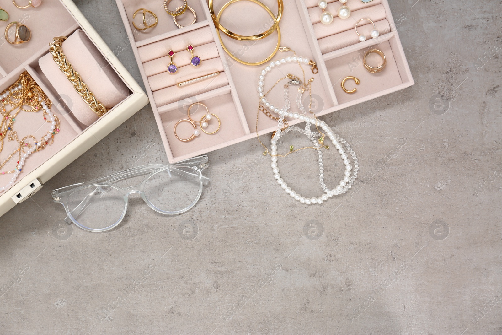 Photo of Jewelry boxes with many different accessories and glasses on light grey table, flat lay. Space for text