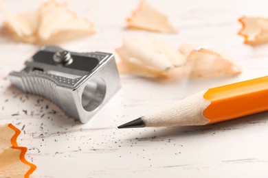Photo of Pencil, sharpener and shavings on white wooden table, closeup