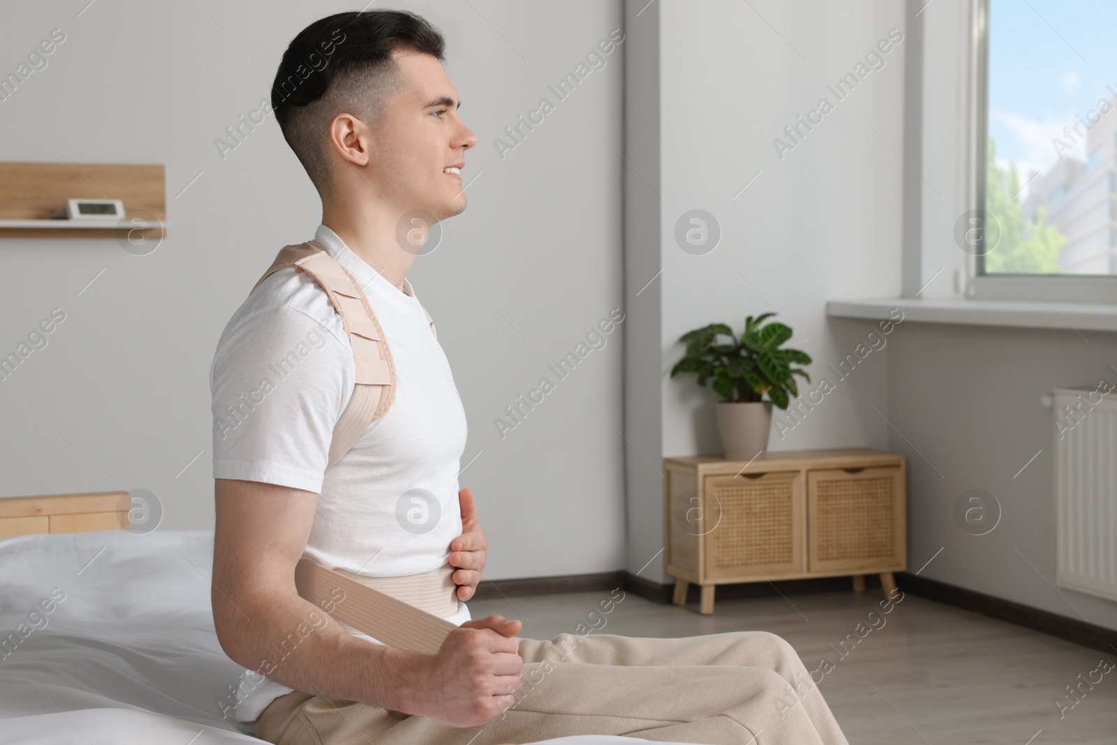 Photo of Handsome man with orthopedic corset sitting in bedroom