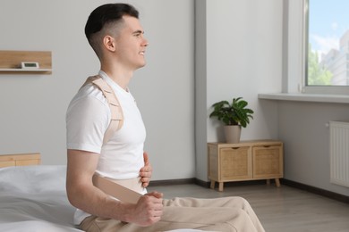 Handsome man with orthopedic corset sitting in bedroom