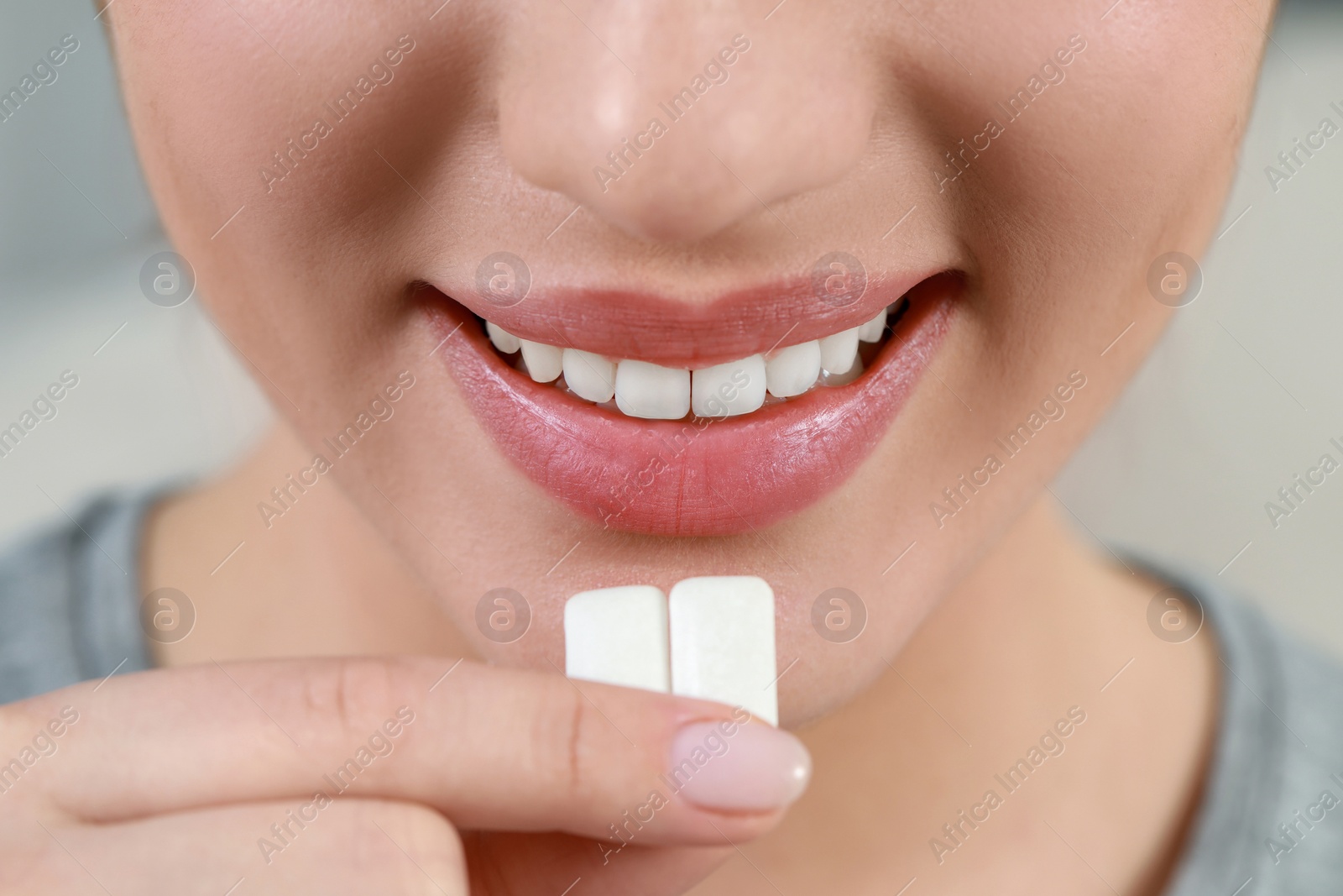 Photo of Woman putting chewing gum pieces into mouth on blurred background, closeup