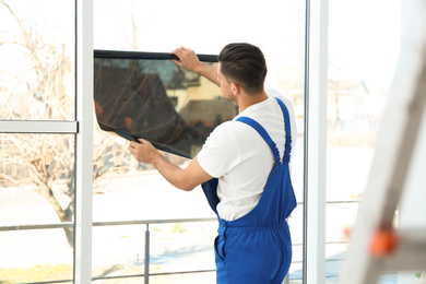Photo of Professional worker tinting window with foil indoors