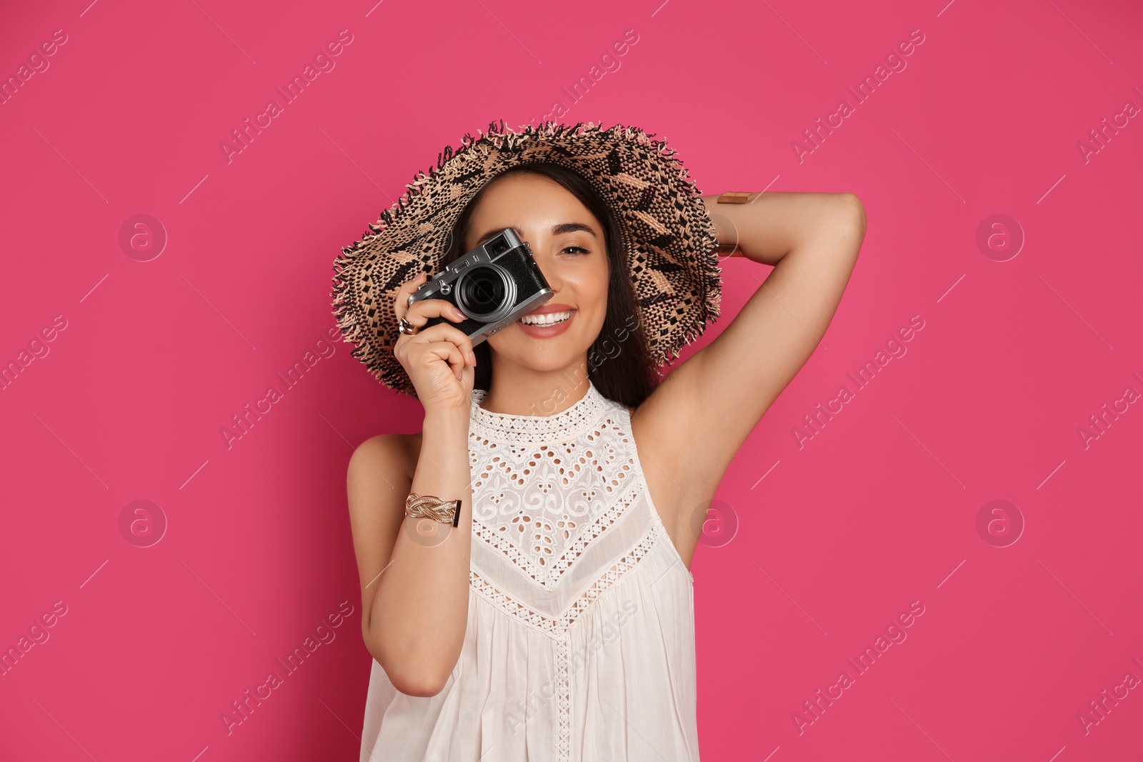 Photo of Beautiful young woman with straw hat and camera on crimson background. Stylish headdress