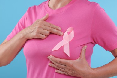 Photo of Woman with pink ribbon on light blue background, closeup. Breast cancer awareness