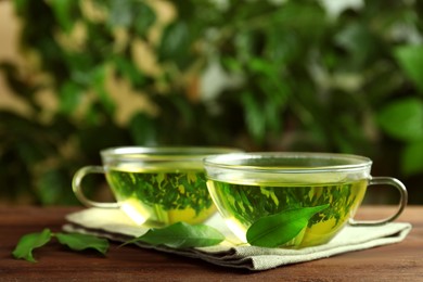 Photo of Fresh green tea in glass cups and leaves on wooden table