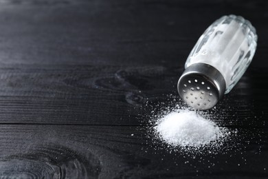 Photo of Organic salt in glass shaker on black wooden table, closeup. Space for text