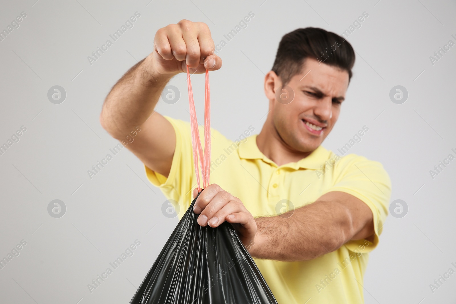 Photo of Man holding full garbage bag against light background, focus on hands