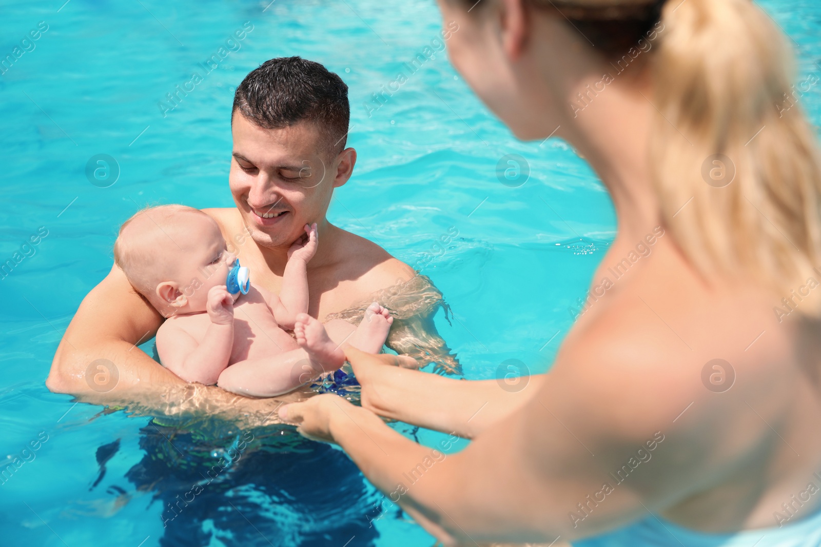 Photo of Happy parents with little baby in swimming pool on sunny day, outdoors