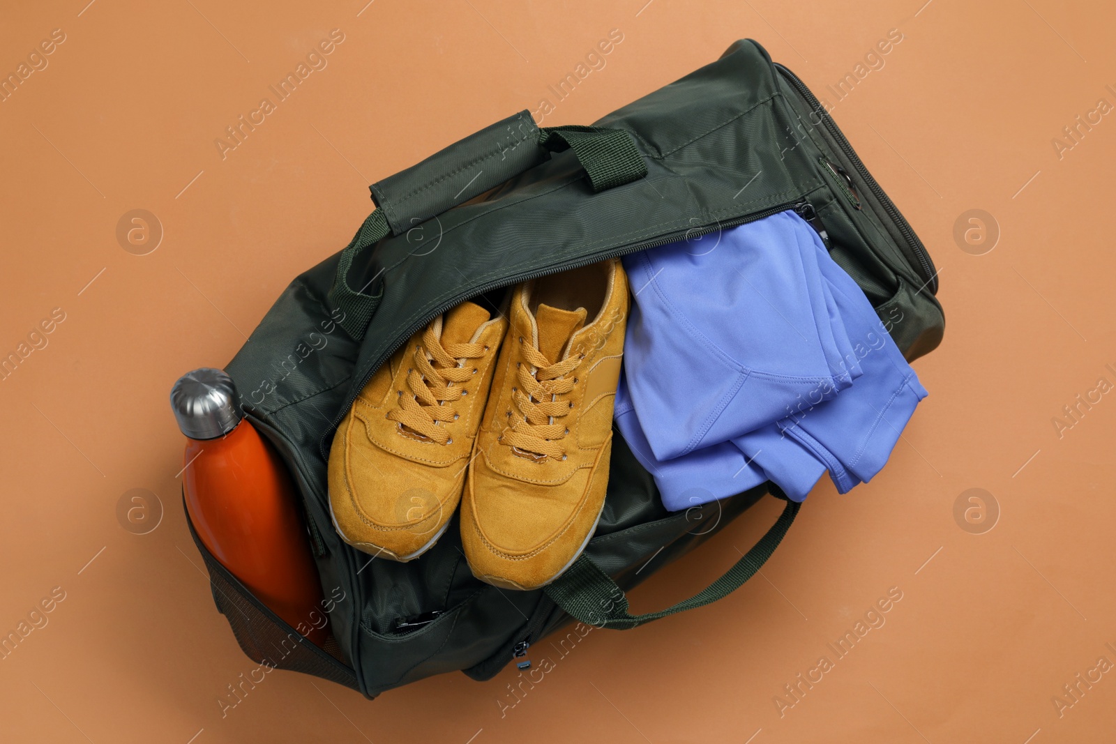 Photo of Sports bag with sneakers, clothes and bottle on pale brown background, top view