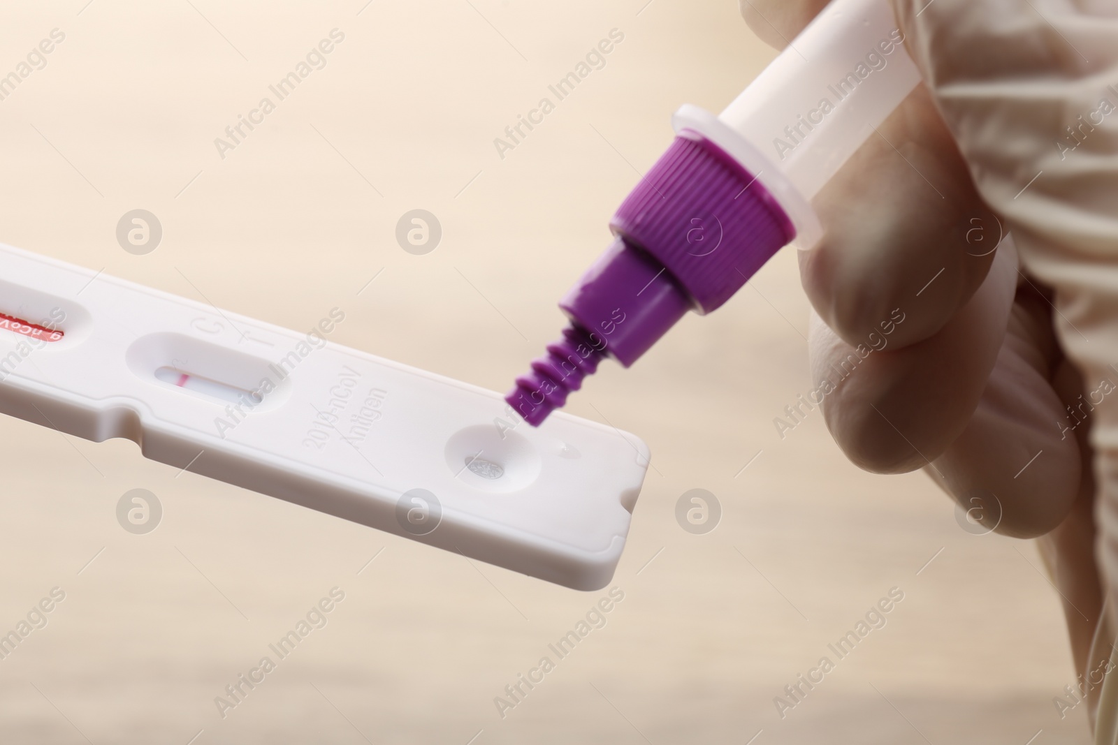 Photo of Doctor dropping buffer solution onto disposable express test cassette against blurred background, closeup