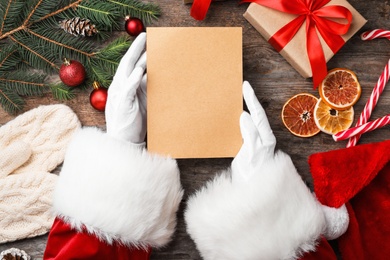 Photo of Santa Claus holding paper and Christmas decor on wooden background, top view