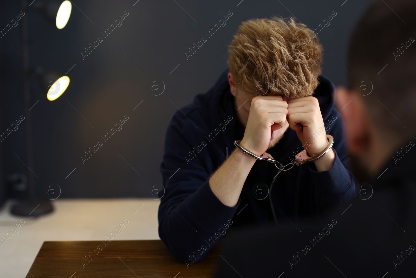 Photo of Police officer interrogating criminal in handcuffs at desk indoors, space for text