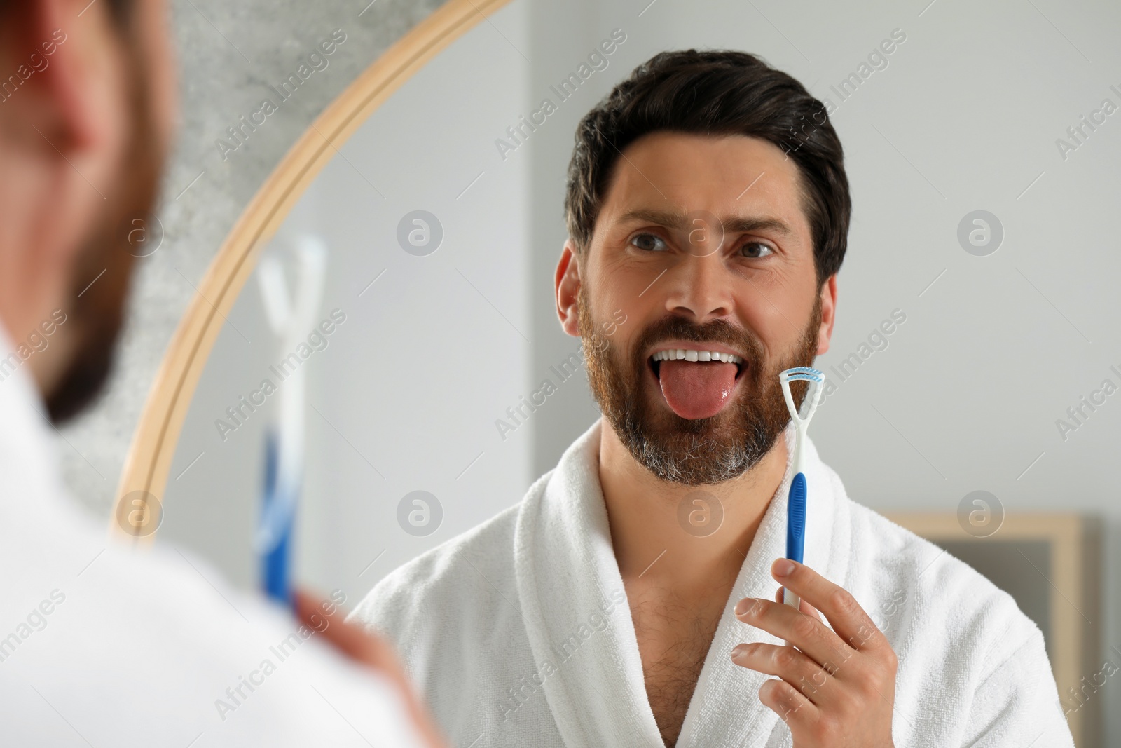 Photo of Happy man with tongue cleaner near mirror in bathroom