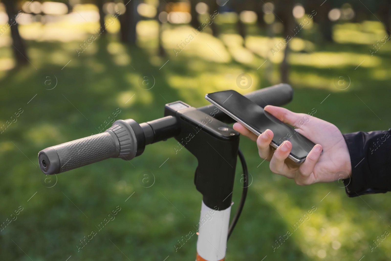 Photo of Man using smartphone to pay and unblock rental electric scooter outdoors, closeup