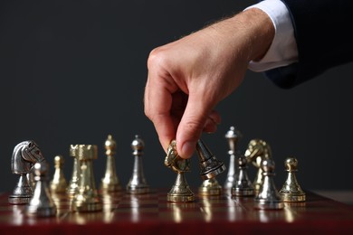 Man with knight game pieces playing chess at board against dark background, closeup