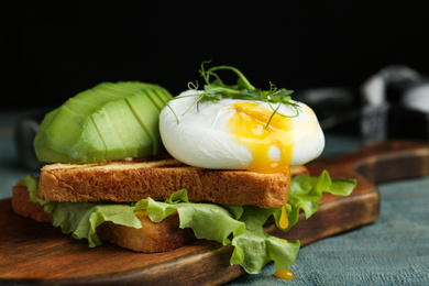 Photo of Delicious poached egg with toasted bread and avocado served on wooden board, closeup