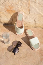 Photo of Stylish sunglasses, slippers and glass of water on stone floor outdoors. Beach accessories