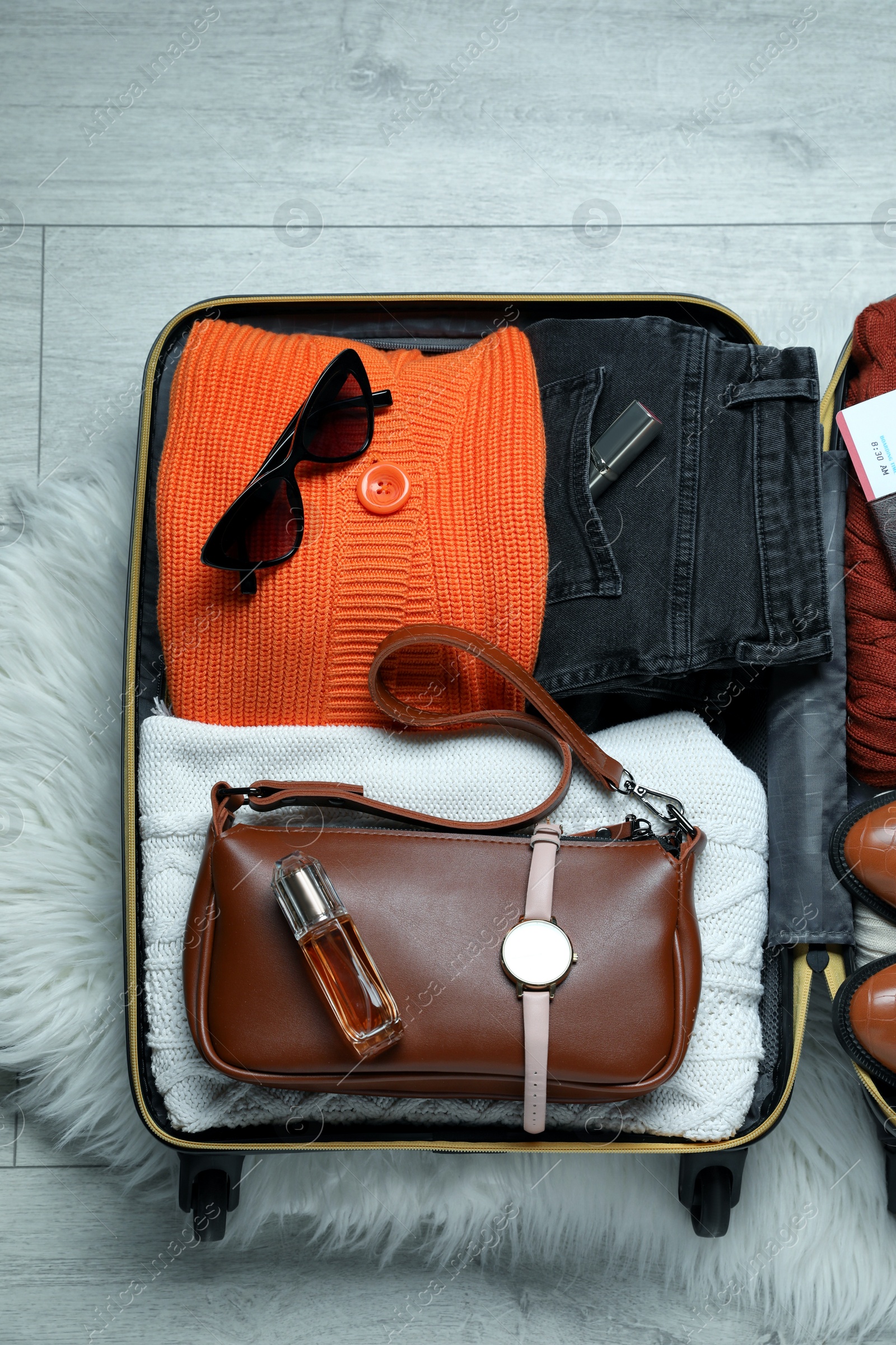 Photo of Open suitcase with folded clothes and accessories on floor, top view