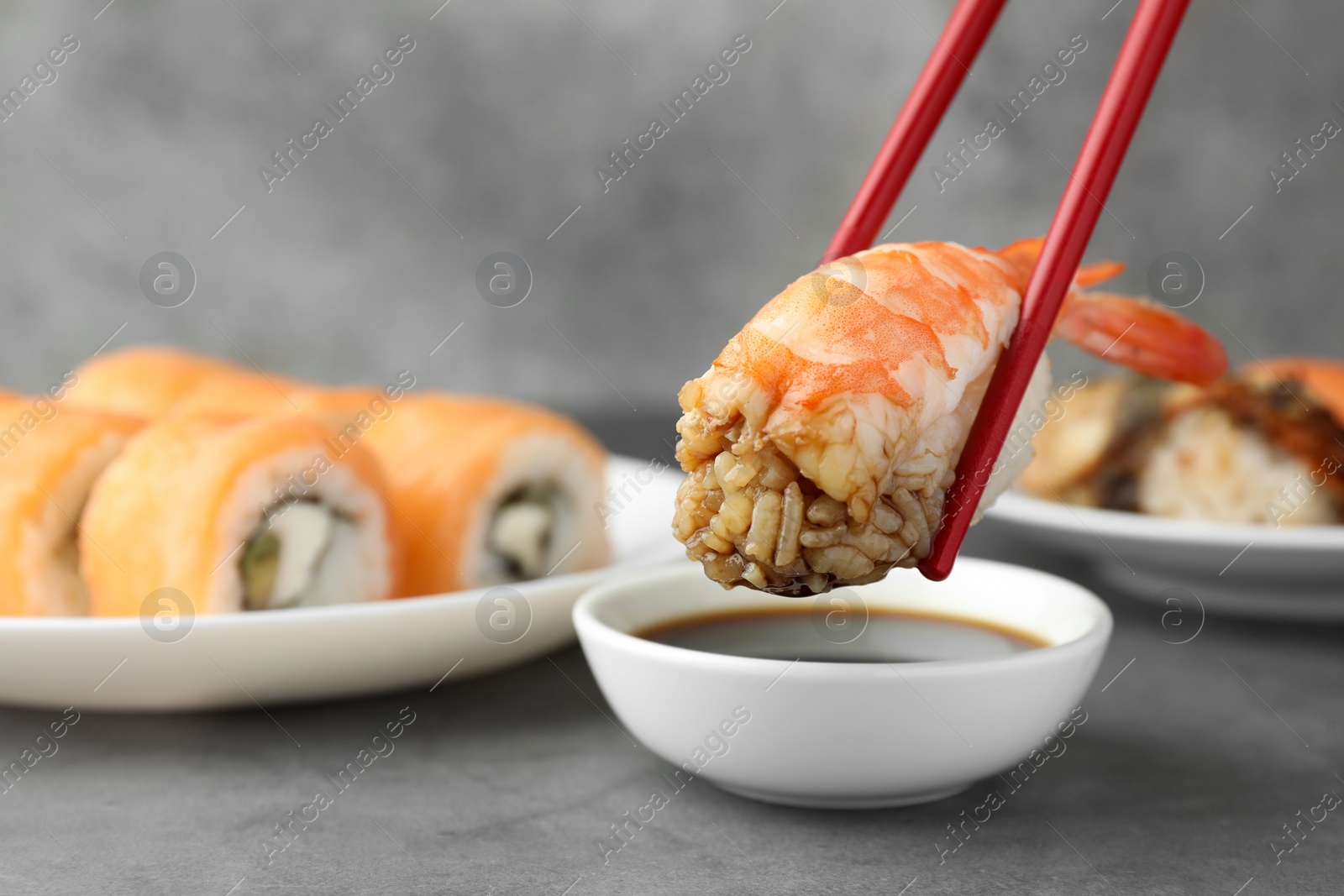 Photo of Dipping tasty nigiri sushi with shrimp into soy sauce on grey table, closeup