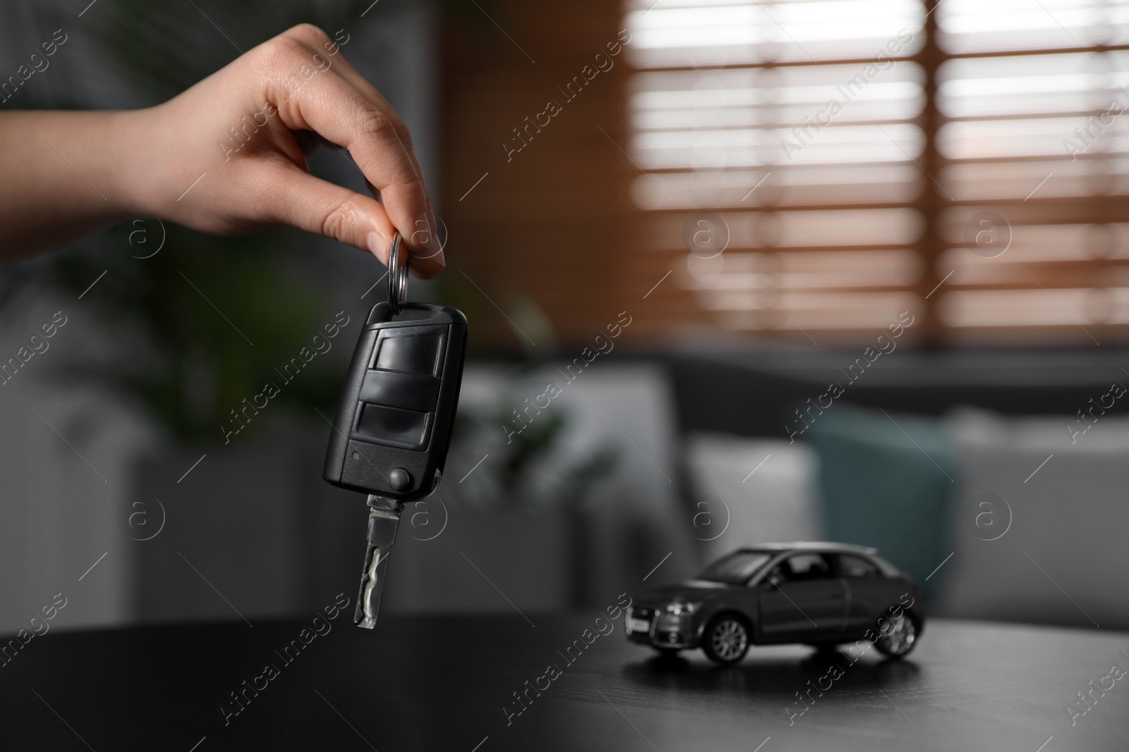 Photo of Man holding key near table with miniature automobile model indoors, closeup. Car buying