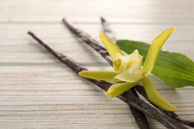 Vanilla pods, beautiful flower and green leaf on white wooden table, closeup. Space for text
