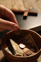 Donate and give concept. Woman putting coin into bowl with money at table, closeup