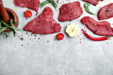 Fresh raw meat steaks and spices on light grey table, flat lay. Space for text