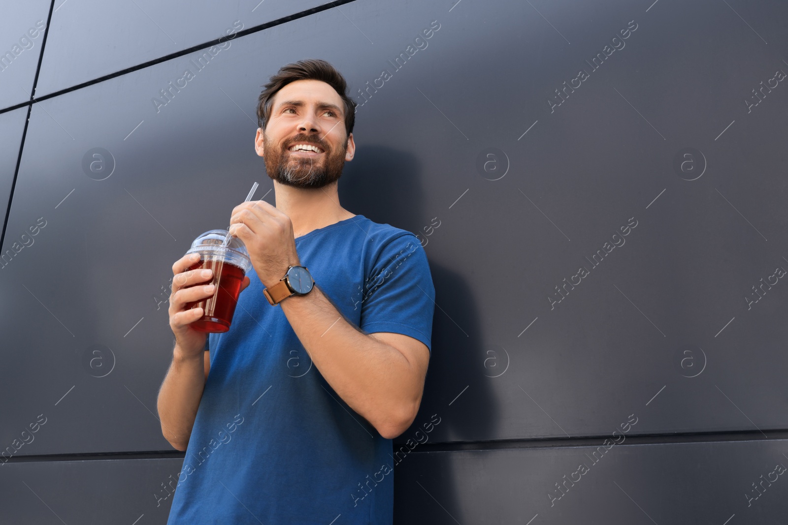 Photo of Happy man with delicious juice near grey wall outdoors, low angle view. Space for text