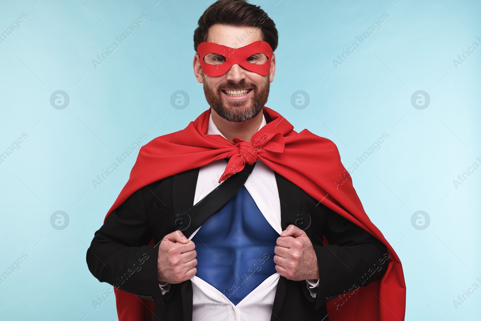 Image of Happy businessman wearing superhero costume under suit on light blue background