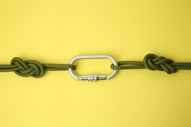 Photo of One metal carabiner with ropes on yellow background, top view