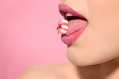 Beautiful young model with creative makeup holding candy in lips on color background