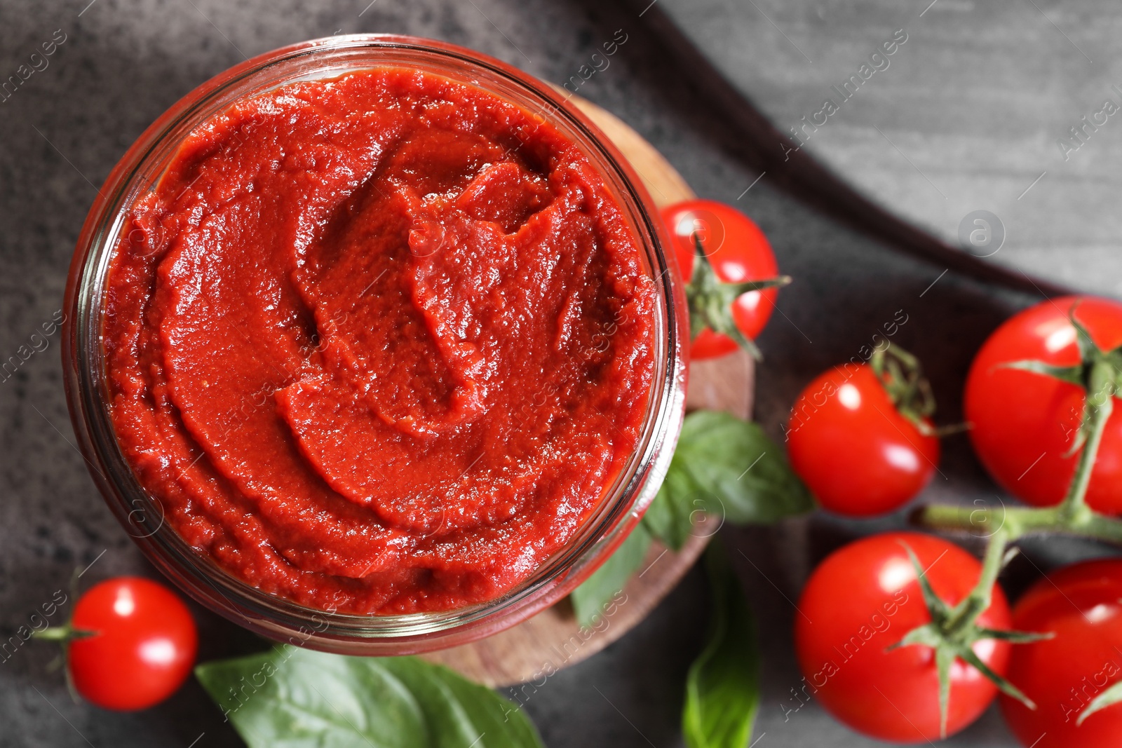 Photo of Jar of tasty tomato paste and ingredients on grey textured table, flat lay. Space for text