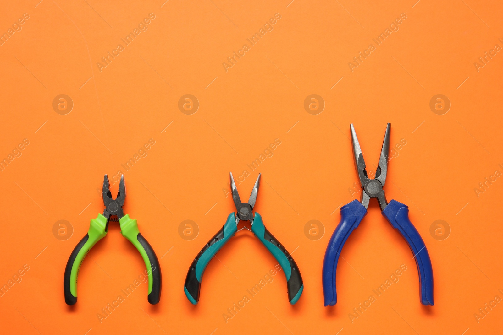 Photo of Different pliers on orange background, flat lay. Space for text